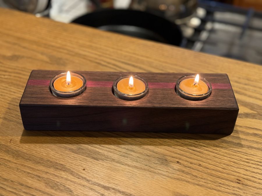 A walnut tealight holder with a purpleheart stripe, three candles lit.