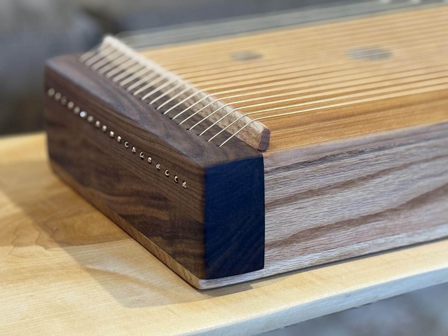 A corner of the monochord where the walnut end block meets the oak side, with strings fanning over the bridge.