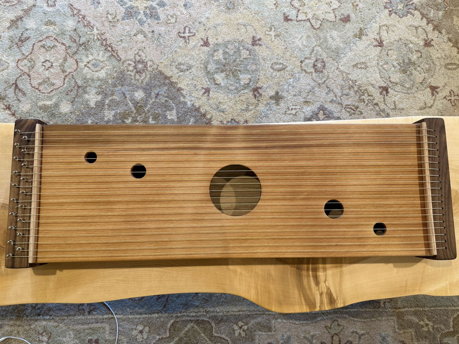 A multi-string monochord seen from above: a cedar soundboard with five round sound holes, strung between walnut end blocks with oak bridges.